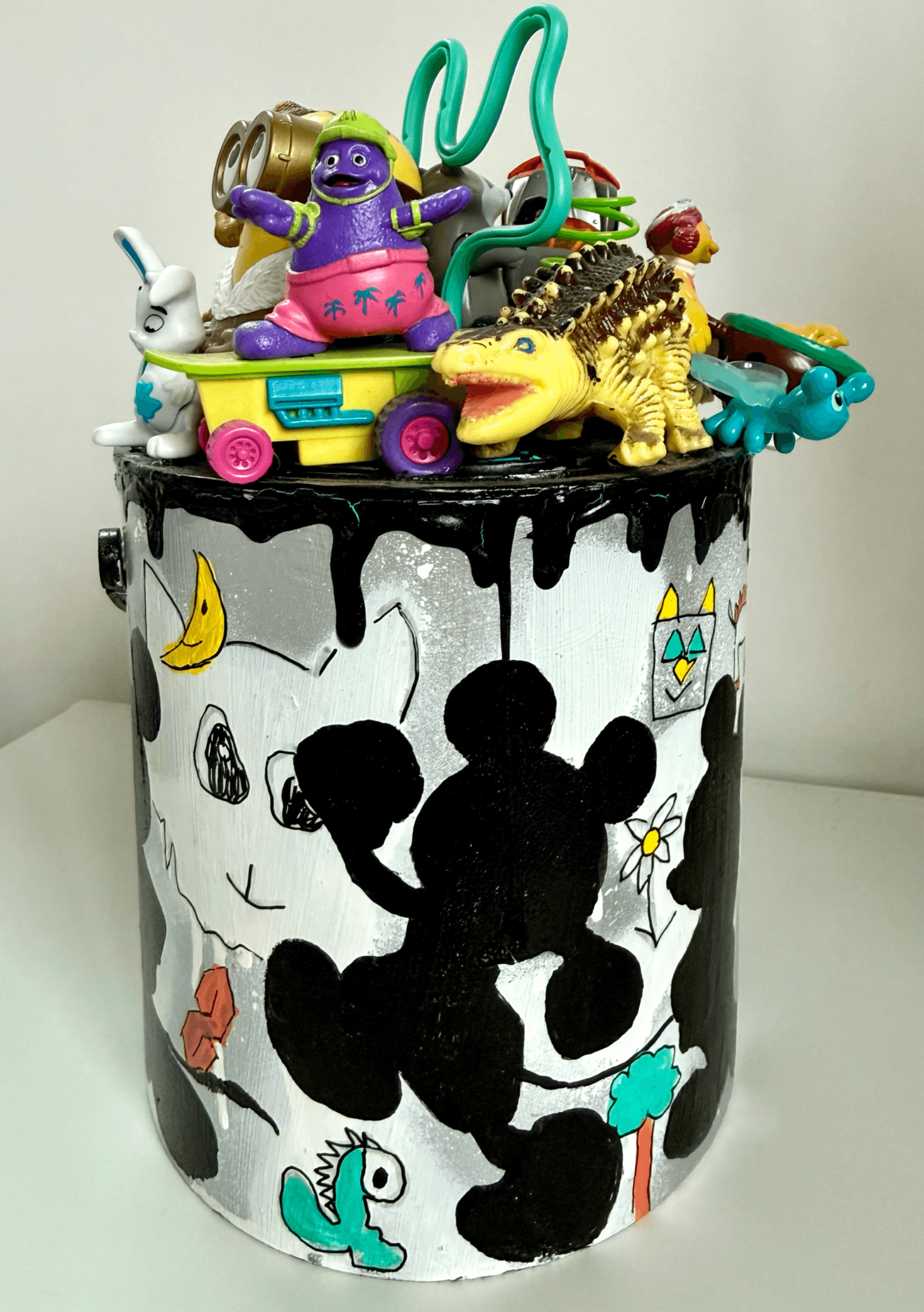 Front view of a recycled paint tin filled with resin-preserved preloved toys and acrylic paint residue.