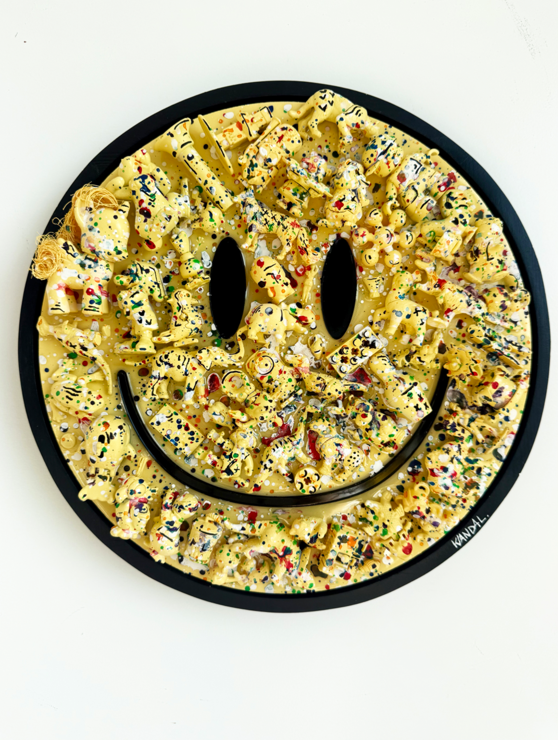 Circular mixed-media assemblage of monochrome toy fragments and resin forming a textured smiley face.